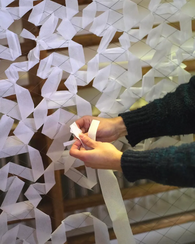 Volunteer weaving fabric strips into a camouflage net