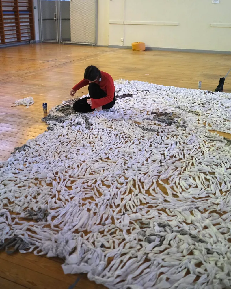 Volunteer working on a large camouflage net in a gymnasium